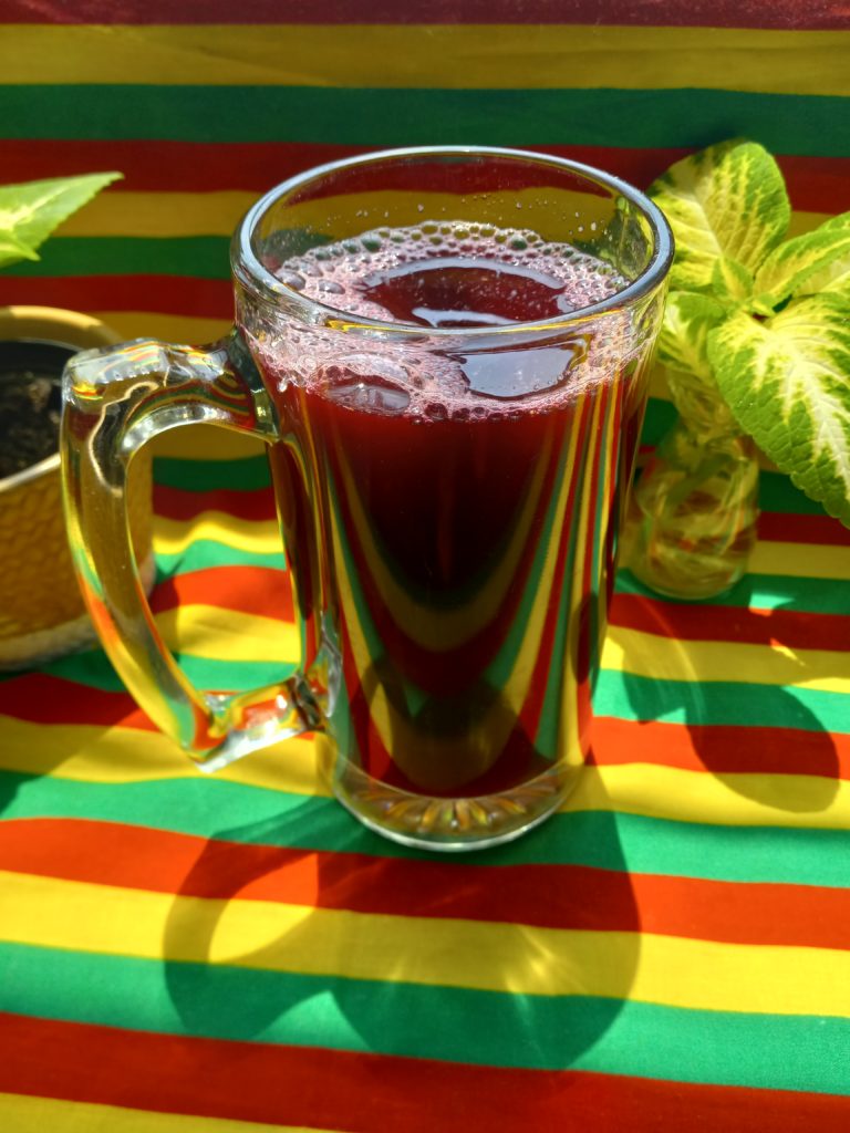 large glass mug with beet and ginger juice on a red, gold, and green background.