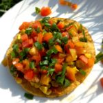chickpea, tomato, and sweet corn tostada on a white plate with green grass in the background