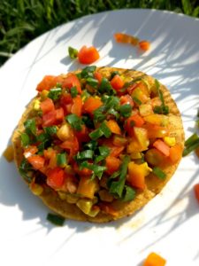 chickpea, tomato, and sweet corn tostada on a white plate with green grass in the background