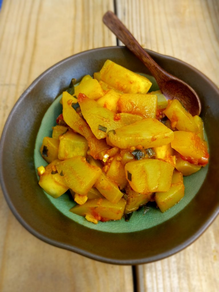 summer recipe #1 a small bowl of zucchini and tomato sauté with a wooden spoon.