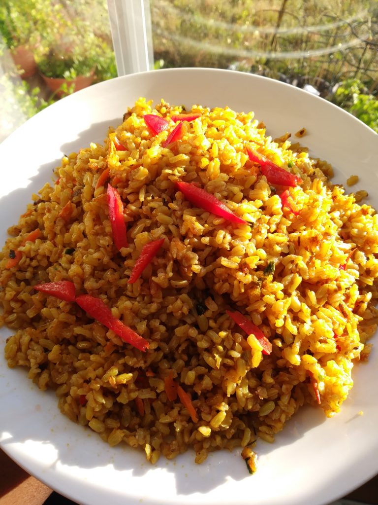 a plate of garlic red bell pepper fired rice with plants in the background