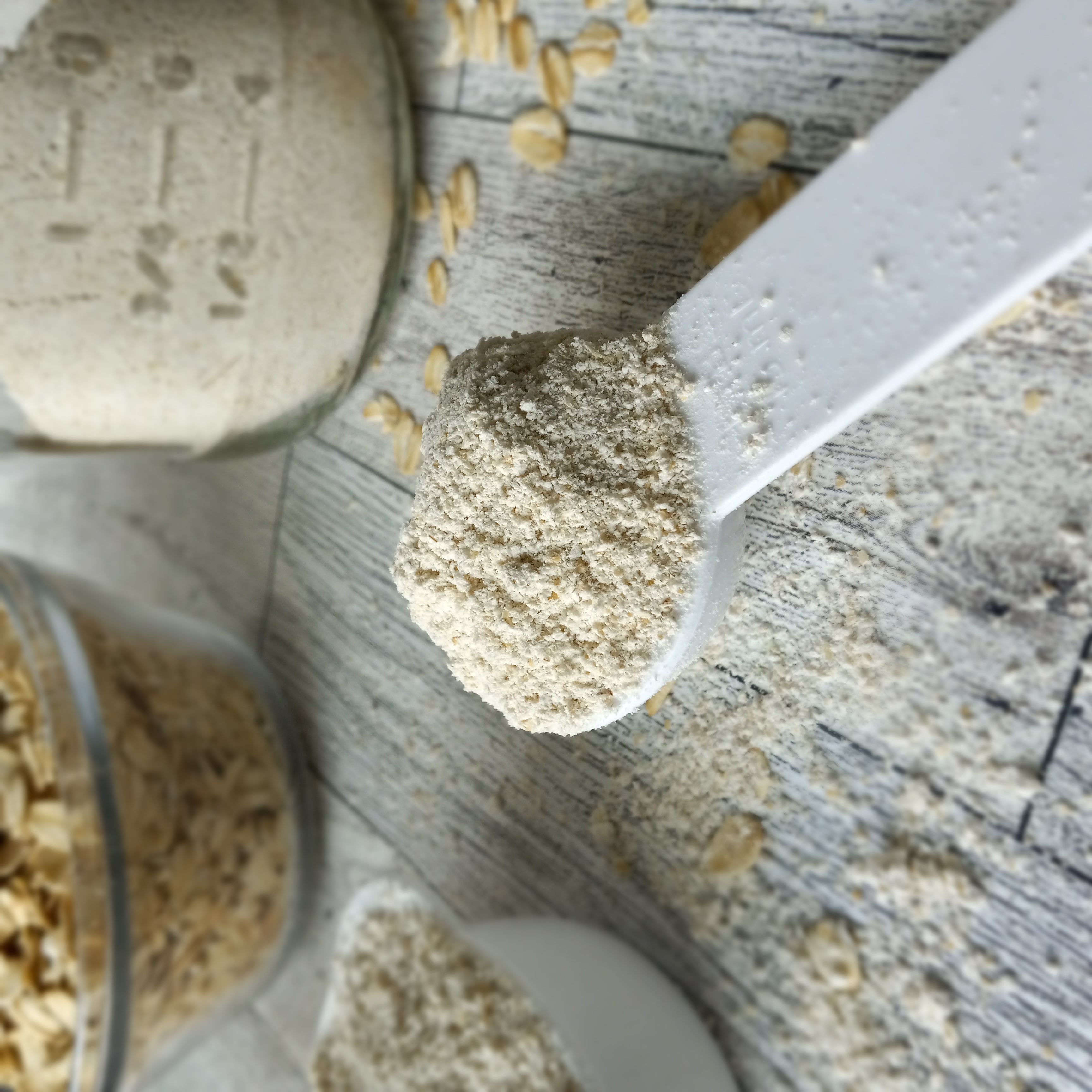 a tablespoon of oat flour with rolled oats and a glass container of oat flour in the background