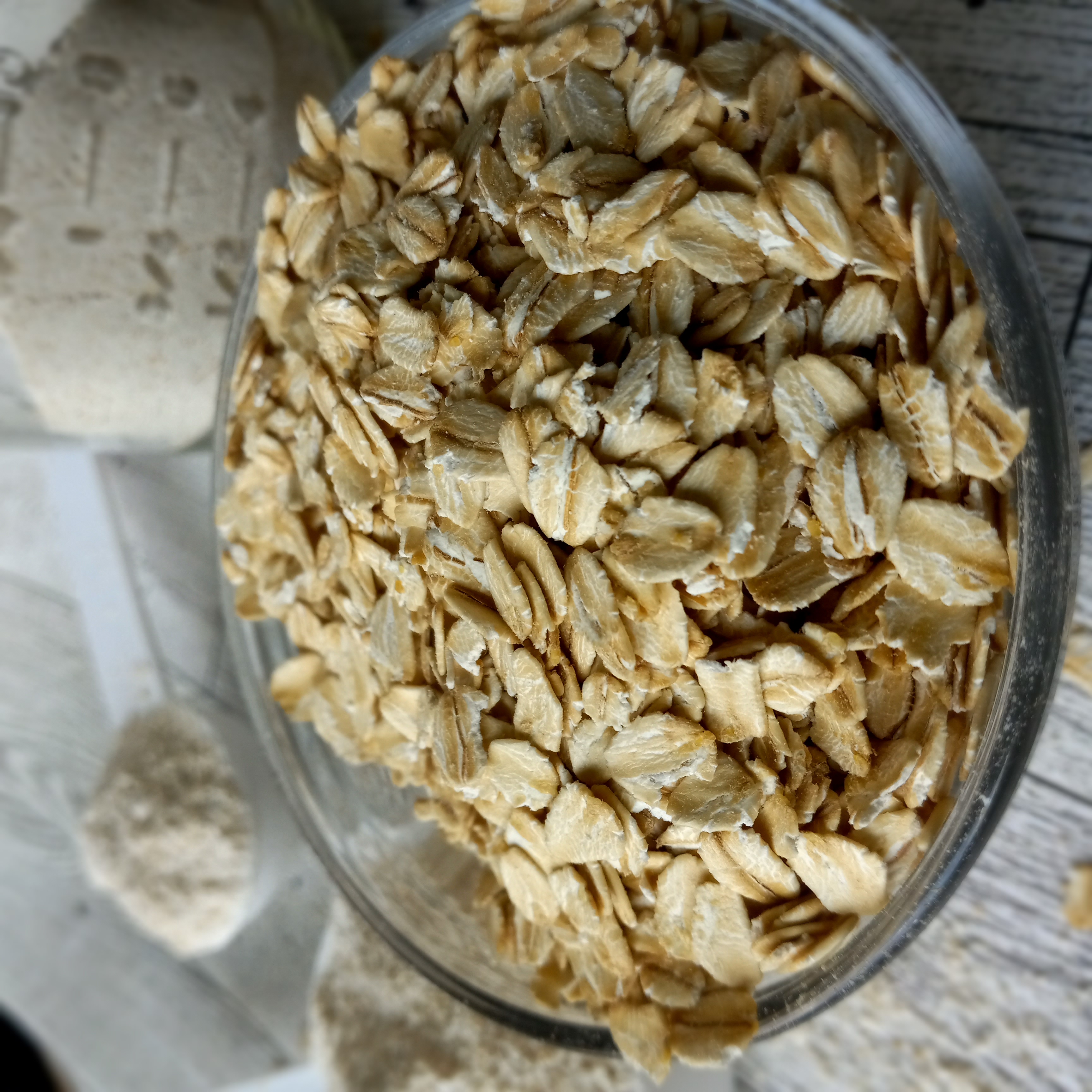 a glass bowl of rolled oats with containers of oat flour in the background