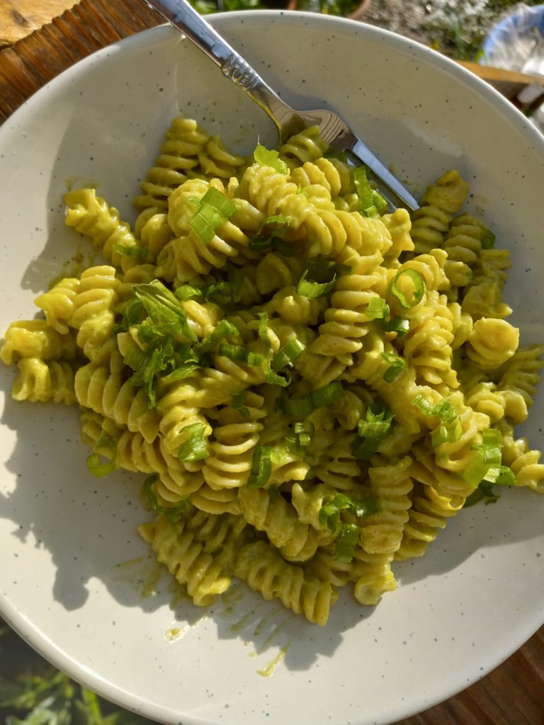 a white plate of creamy avocado pasta with tahini and green onions.