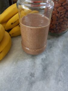 glass jar of homemade almond butter with raw almonds and bananas in the background.