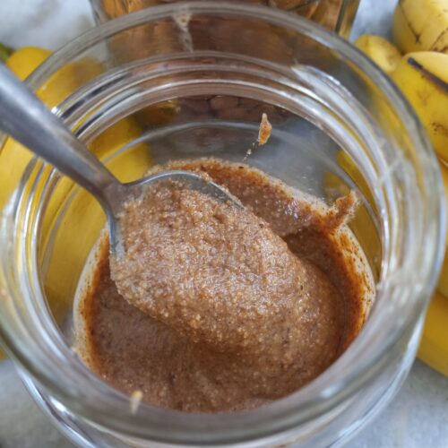 a glass jar of almond butter with a spoon inside.