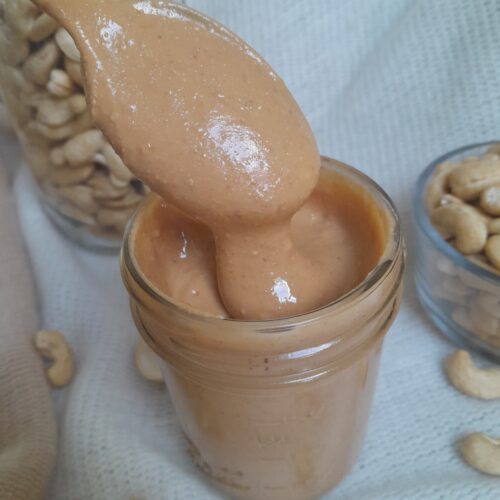 glass jar of cashew butter with raw cashews in the background