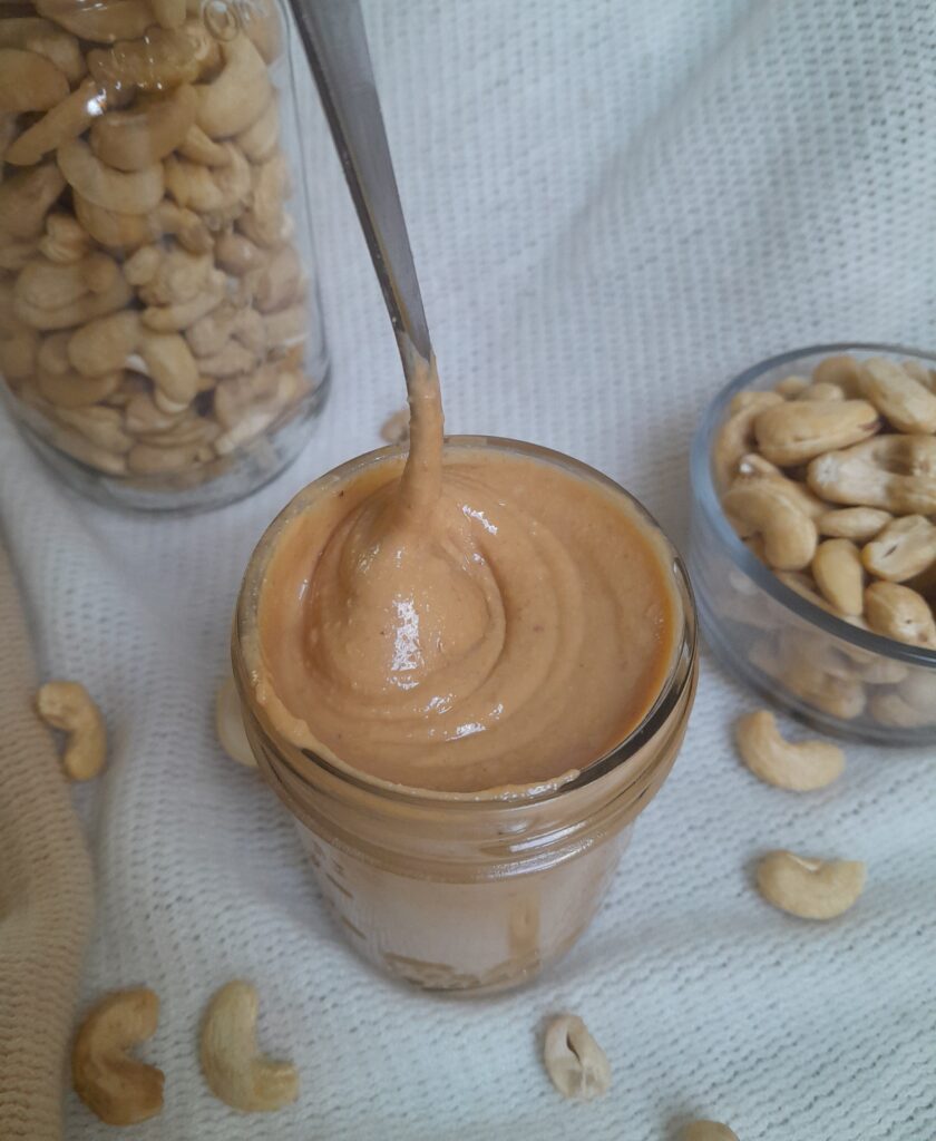 jar of cashew butter with a metal spoon and raw cashews in the background