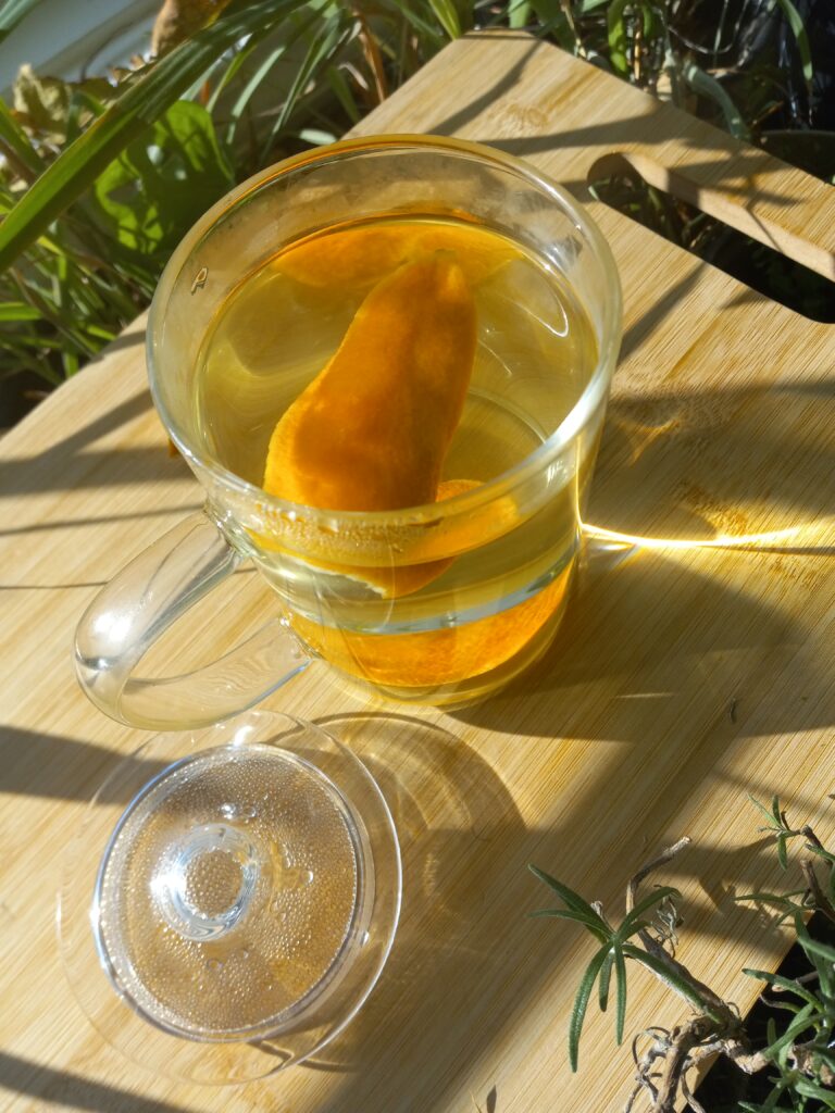 Glass mug of Immunity Boosting Orange Peel Tea on a wooden cutting board with plants in the background.