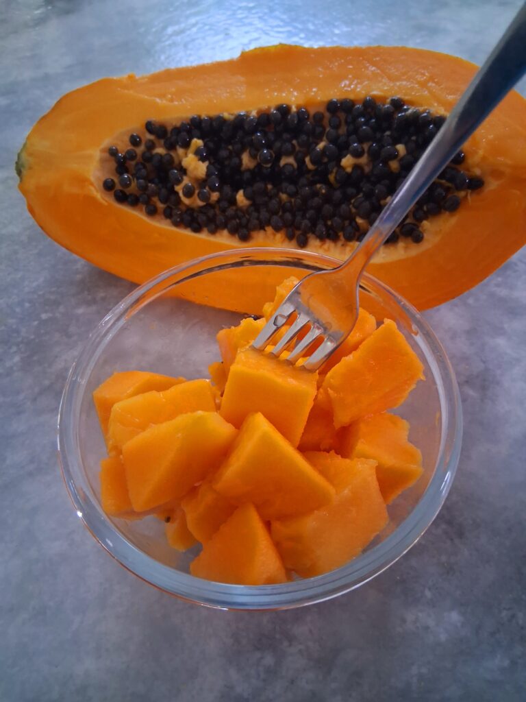 glass bowl of fresh cubed papaya with a half of papaya with the seeds